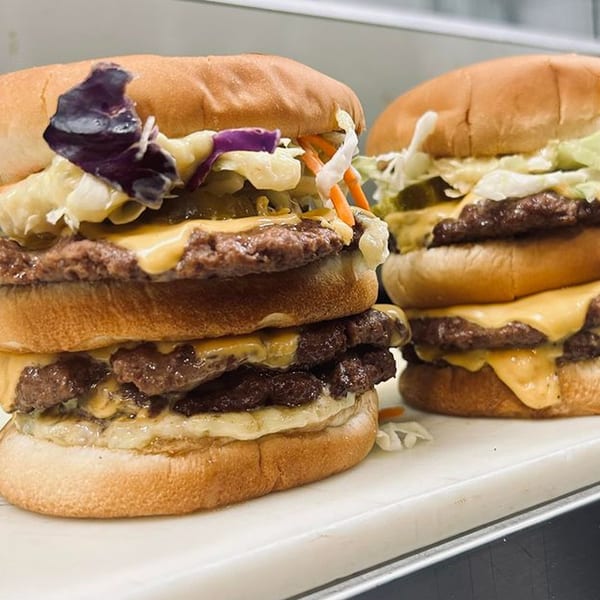 Two double-patty cheeseburgers from The Burger Bunker, topped with coleslaw and purple cabbage.