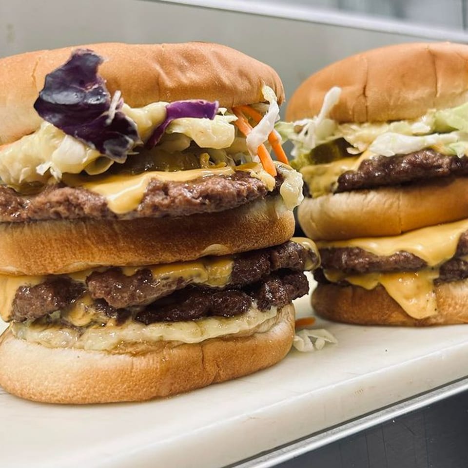 Two double-patty cheeseburgers from The Burger Bunker, topped with coleslaw and purple cabbage.