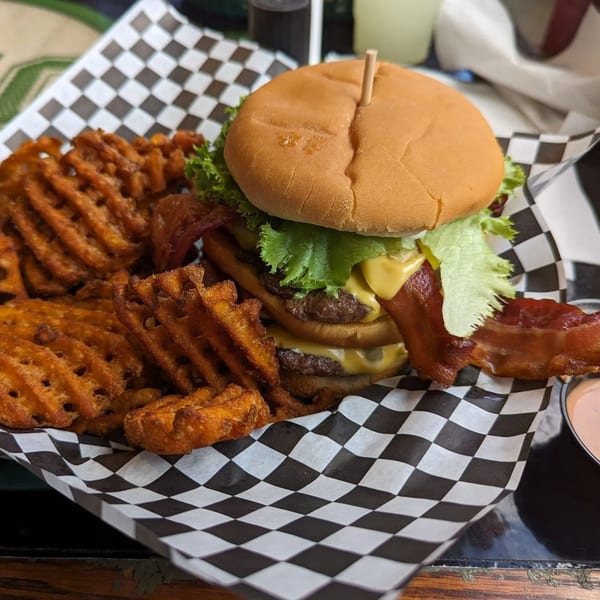 Double cheeseburger with bacon, lettuce, and waffle fries on checkered paper at The Burger Bunker.