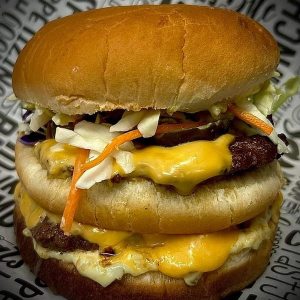 A double-patty Burger Bunker burger with melted cheese, coleslaw, and carrots on a bun.